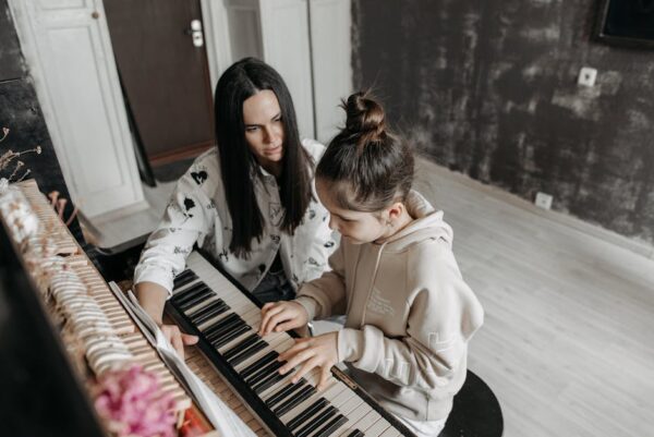 A music teacher helps a young girl learn piano in a cozy indoor studio setting.