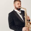 Man in a black suit playing a saxophone in a studio setting, exuding elegance.