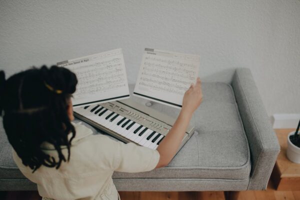 A young girl sits indoors playing an electronic keyboard with music sheets.
