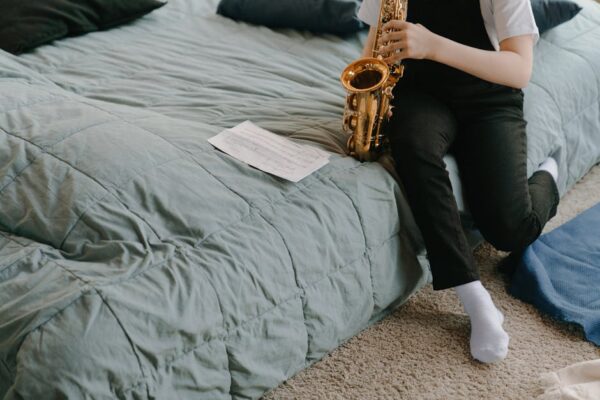 A child sitting on a bed playing a saxophone with music sheets in a cozy bedroom setting.