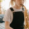 A young girl plays the saxophone indoors, showcasing musical talent.