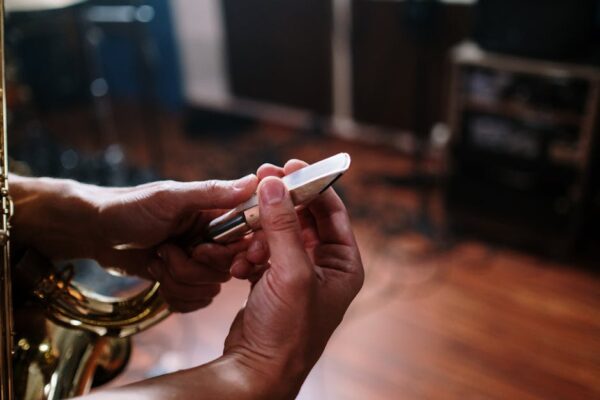 Detailed view of hands fine-tuning a saxophone mouthpiece in a music studio.