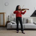 Young woman practicing violin in stylish living room, creating an artistic and musical atmosphere.