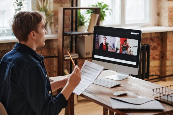 Adult male taking an online violin lesson with sheet music and computer.