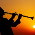 Silhouette of a musician playing clarinet against a vibrant sunset sky.