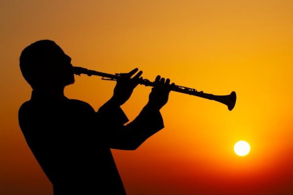 Silhouette of a musician playing clarinet against a vibrant sunset sky.