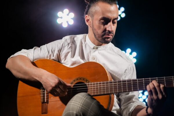 Portrait of a man playing acoustic guitar onstage with dramatic lighting.