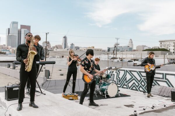 A diverse music band plays on a rooftop with city skyline in the background.