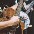 Close-up of musicians strumming acoustic and banjo guitars in a vibrant street performance.