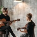 A man teaching a boy to play the acoustic guitar in an indoor setting.