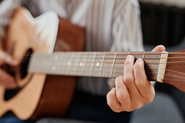 A person strumming chords on an acoustic guitar, focusing on fretboard technique.