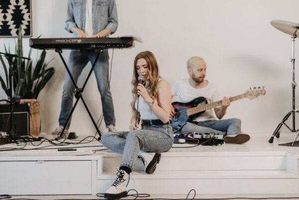 Young band members rehearsing indoors with instruments and a vocalist.