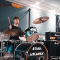 A young drummer practicing with a band in a modern music studio.