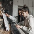 Young girl learning piano with her teacher in a music studio, focusing on sheet music.