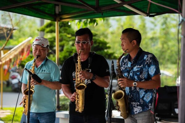 Three male musicians play saxophones outdoors under a tent, creating a lively and joyful atmosphere.