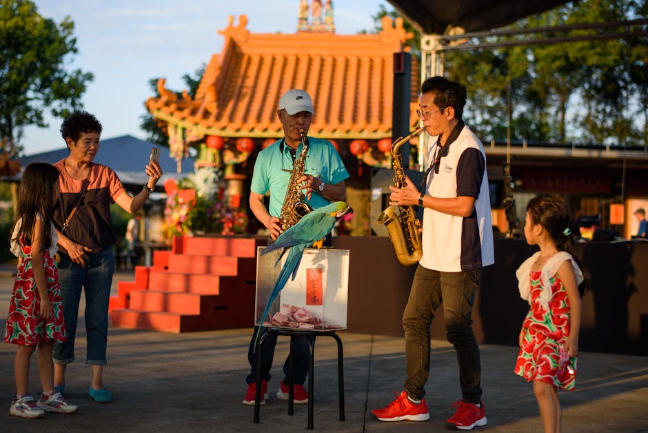 Two saxophonists entertain a family with bright parrots in an urban setting.