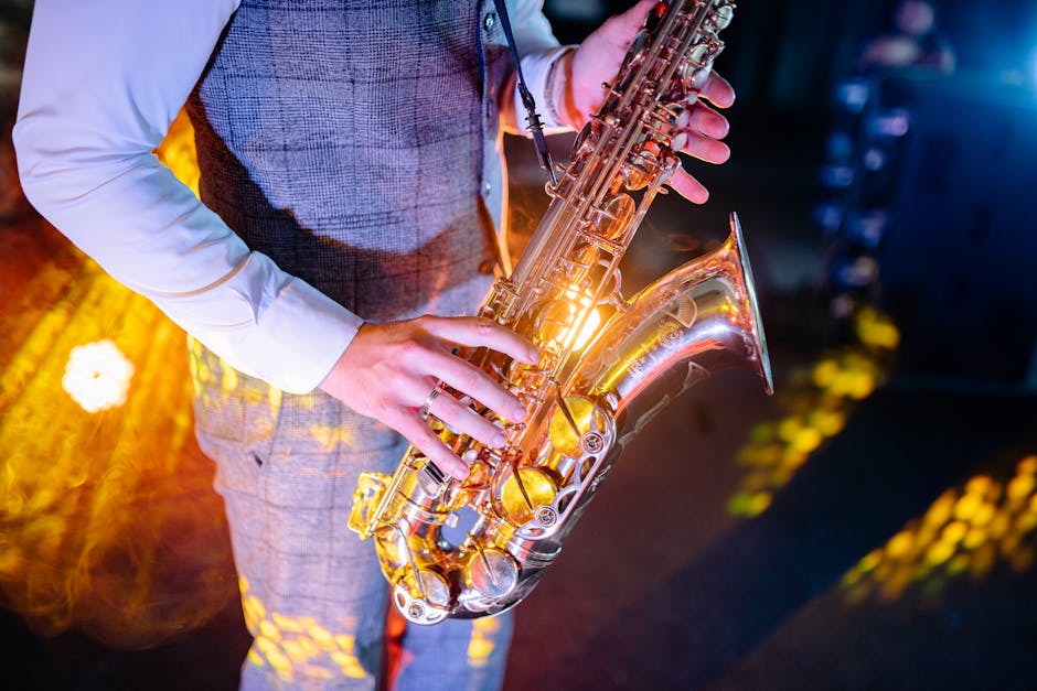 Close-up of a musician's hands playing a saxophone under colorful stage lights.