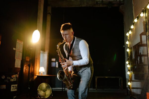 Musician plays saxophone in dimly lit room, creating moody jazz ambiance.