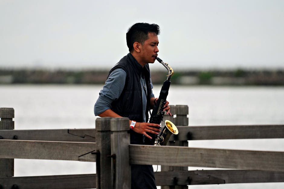 A man passionately plays saxophone on a wooden pier by the water, creating music in nature.