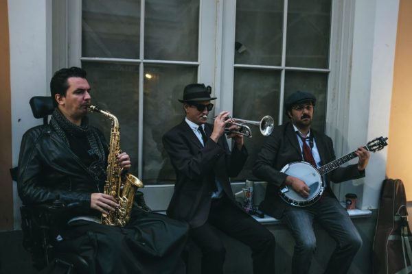 Three street musicians perform with saxophone, trumpet, and banjo.