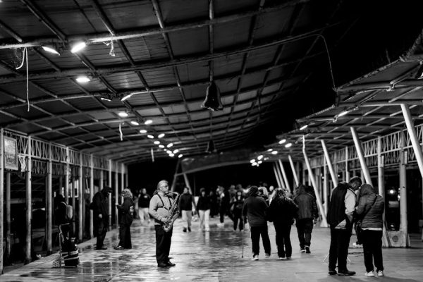 A black and white image of a saxophonist playing at a bustling night market.