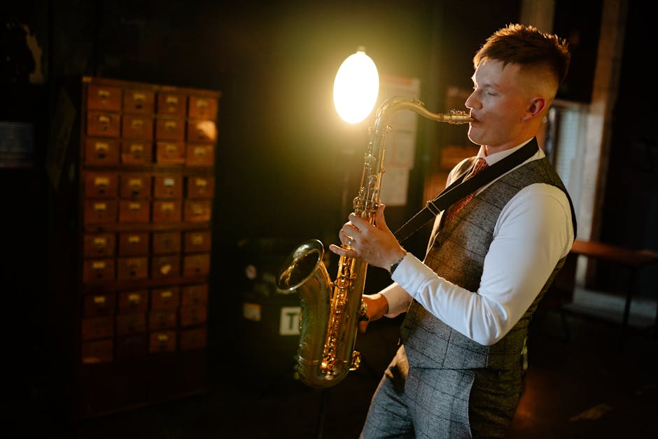 Young male saxophonist in a stylish suit performing under a spotlight indoors.