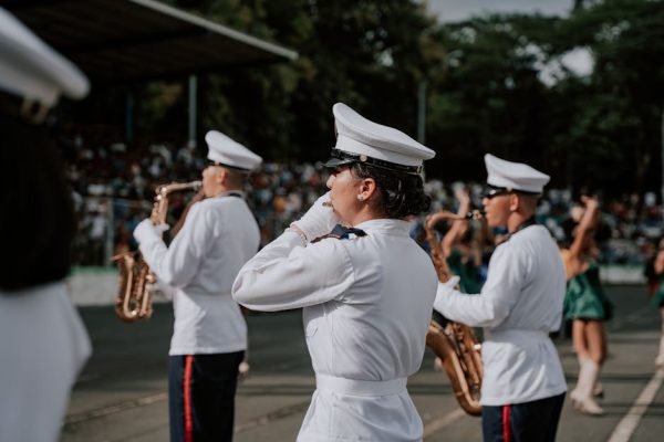 Military band playing in a parade with musicians in white uniforms and saxophones outdoors.