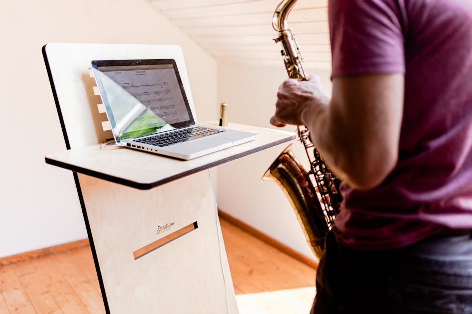 A musician practices saxophone using a laptop on a modern wooden stand indoors.
