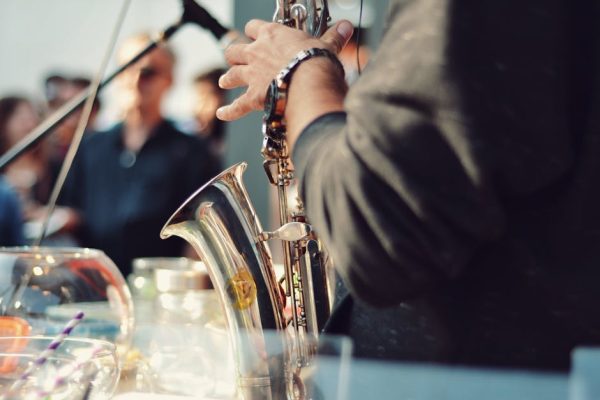 A saxophonist playing music at an event with an audience in the background.