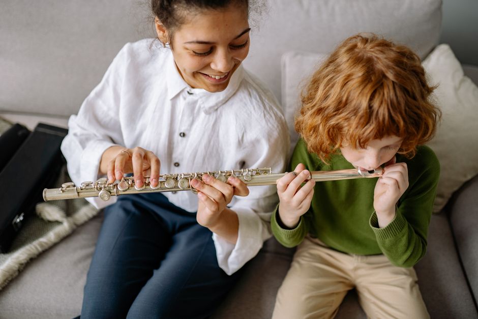 Young boy learning to play flute with a woman teacher on a sofa, indoors.