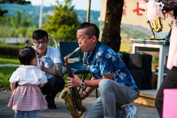 Asian musician playing saxophone outdoors entertaining a child.