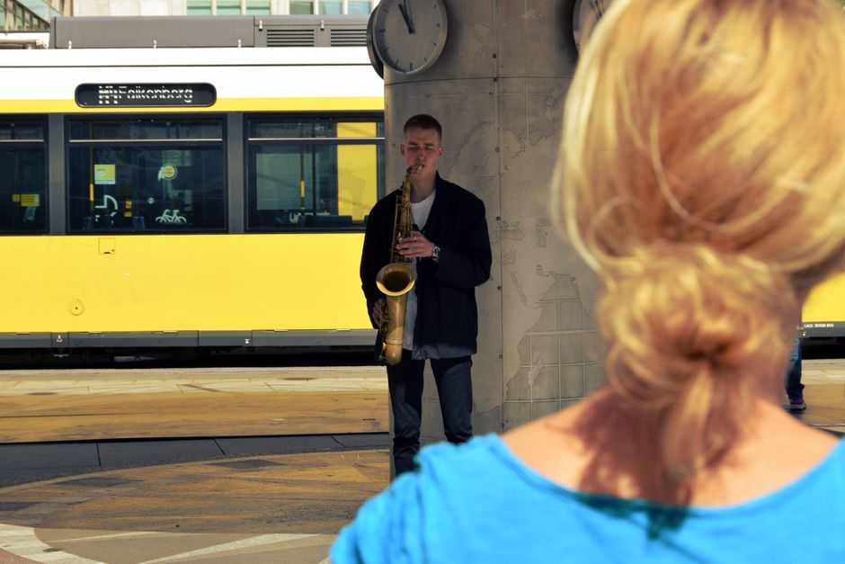 A saxophonist performs on a Berlin platform, adding musical charm to the busy station environment.