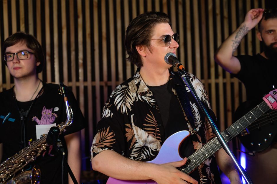 A lively band rehearsing with guitar, saxophone, and vocals in a music studio.