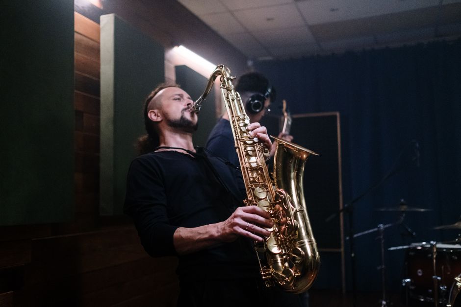Musician playing saxophone passionately in an indoor recording studio setting.
