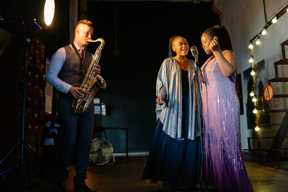 A vibrant stage performance featuring a saxophonist and two singers in elegant attire.
