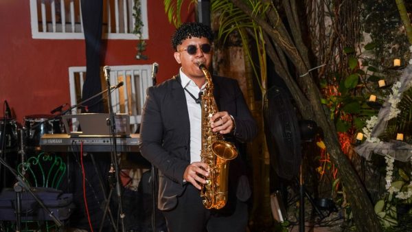 A saxophonist performs at an outdoor evening music event, surrounded by instruments.
