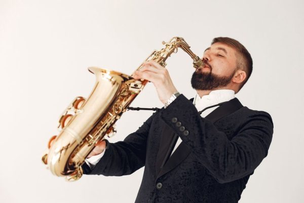 A passionate saxophonist performs in a stylish black suit against a neutral background.