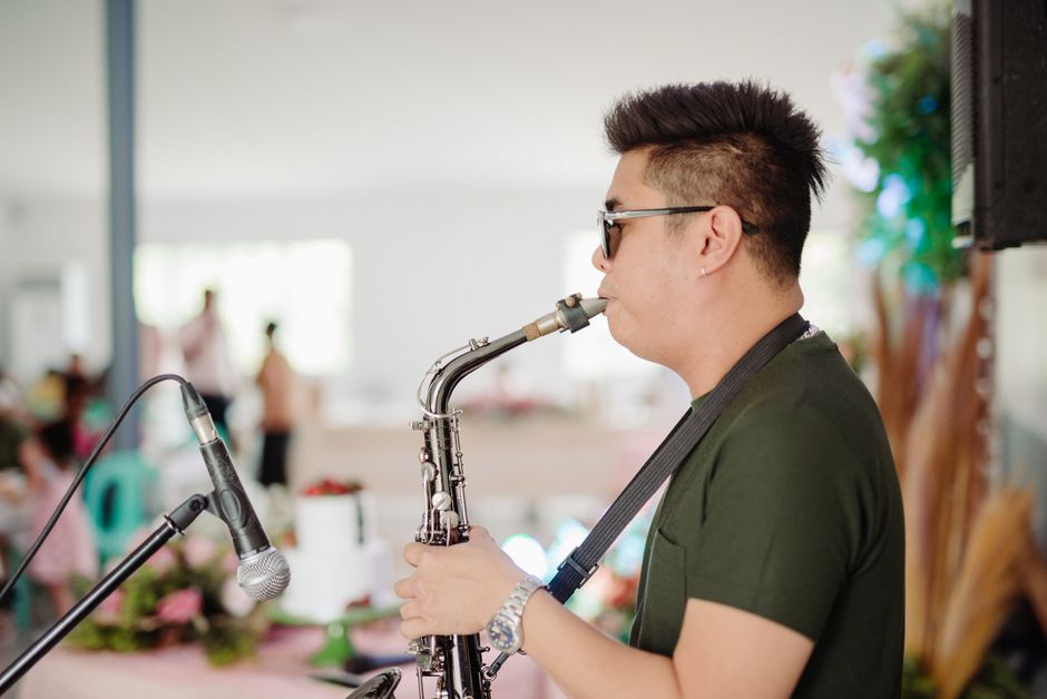 Musician performing with saxophone at an indoor gathering, blurred background
