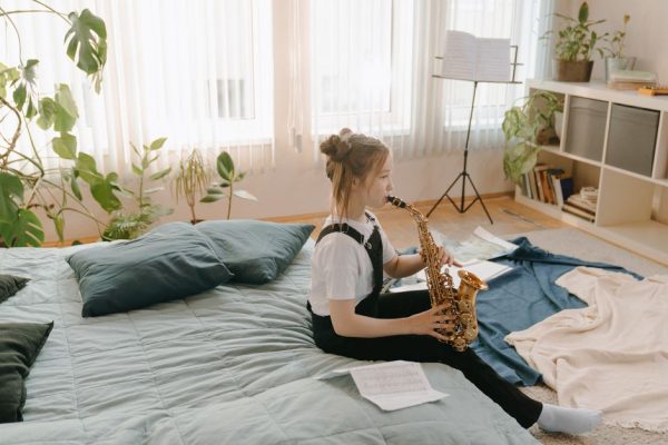 A young girl practices the saxophone in a cozy indoor setting, surrounded by musical sheets and plants.