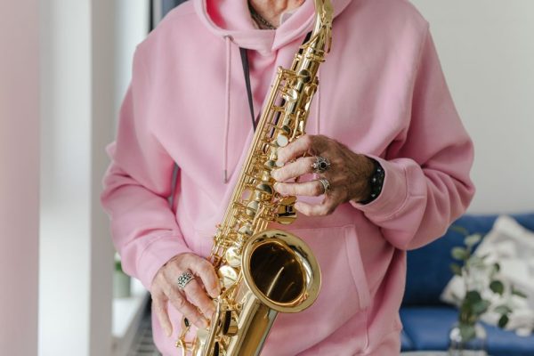 A musician plays a saxophone while wearing a pink hoodie indoors.