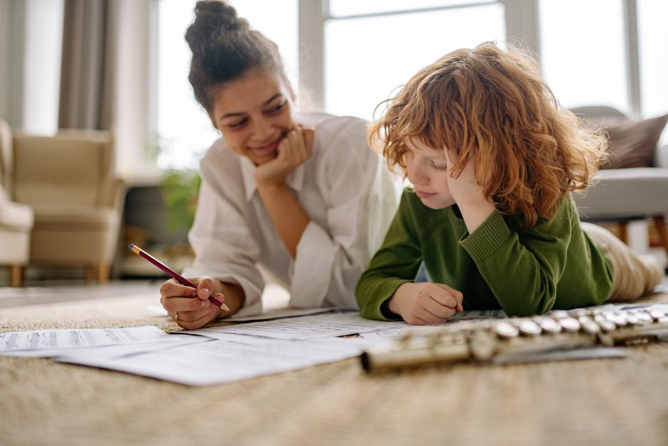 A young boy learning to play the flute at home with a music teacher, focusing on music sheets.