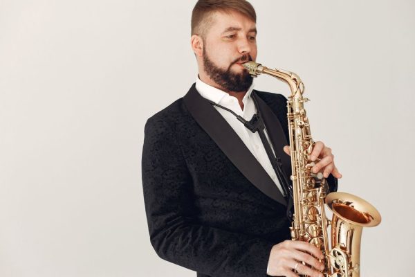 Man in a black suit playing a saxophone in a studio setting, exuding elegance.