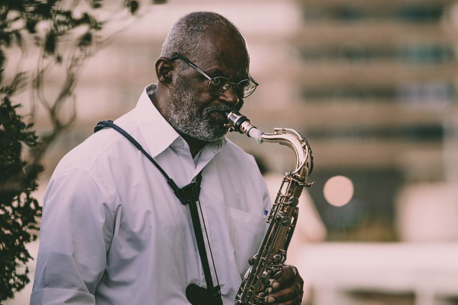 An elderly musician playing a saxophone outdoors in a serene setting.