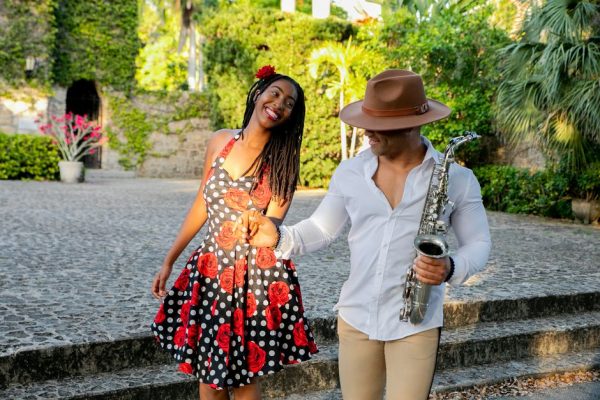 Joyful interracial couple dancing and holding hands outdoors, with a saxophone in hand, engaging in a fun moment.