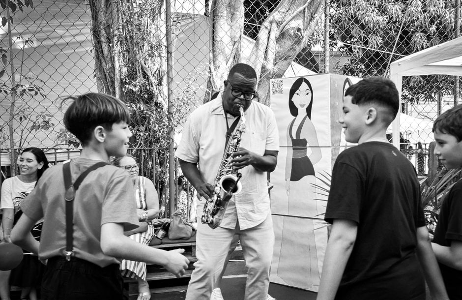 A vibrant street scene with a saxophonist entertaining children outdoors in monochrome.