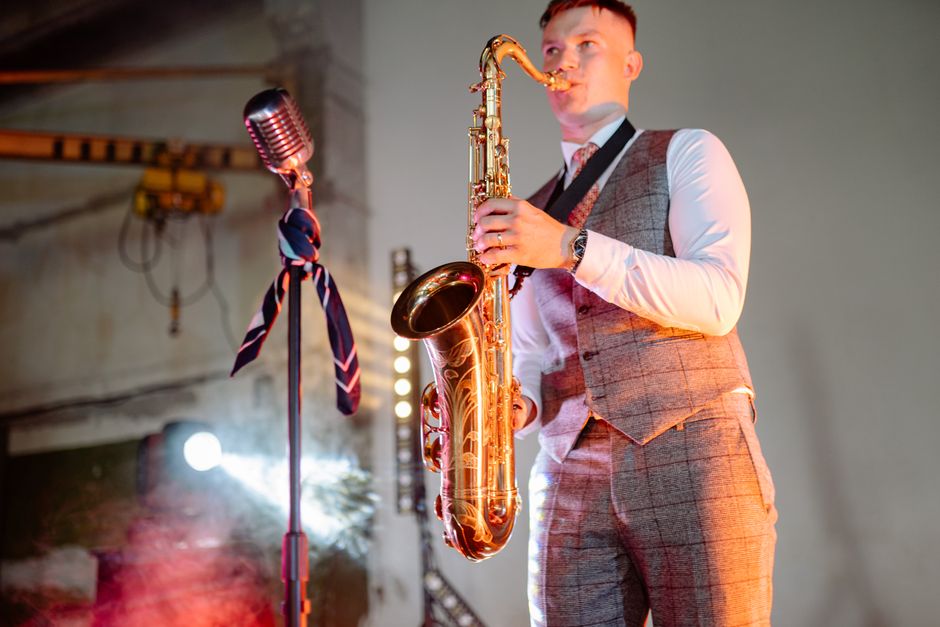 A saxophonist playing live music indoors with a vintage microphone on stage.