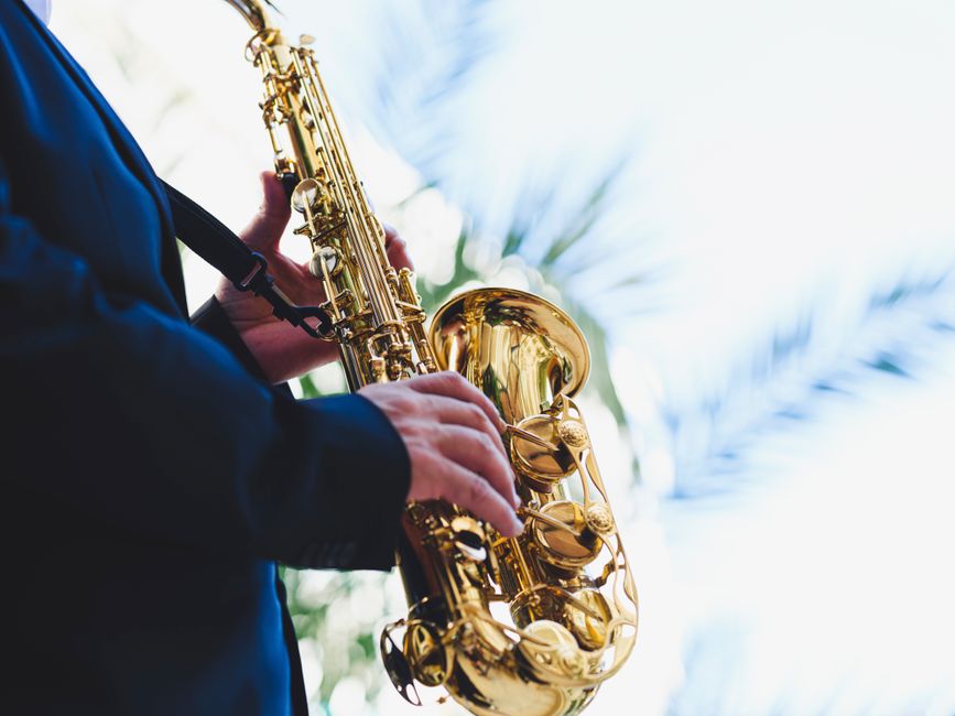 A musician in a suit plays a golden saxophone against a bright sky, showcasing musical talent and outdoor ambiance.