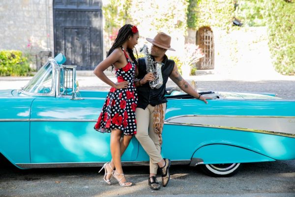 Stylish couple with saxophone by a classic car. Nostalgic and vibrant scene.