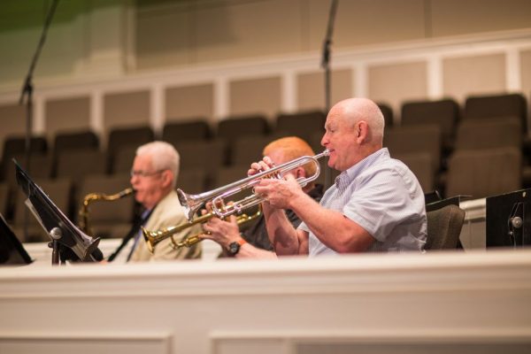 A group of senior adults performing with brass instruments indoors during a concert.