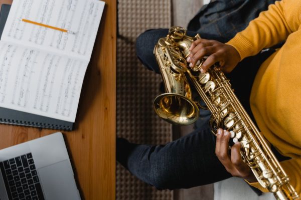 Close-up of a person playing saxophone next to open sheet music and a laptop.
